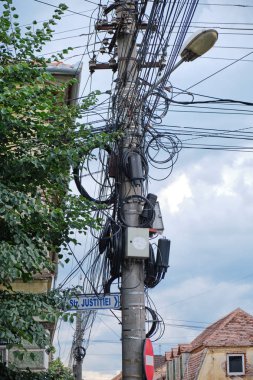 Sibiu, Romanya'daki Justice Street'te (Strada Justitiei) at - Düzensiz bir konuda ondan sarkan Tv, internet, telefon ve elektrik kabloları ile sokak direği.