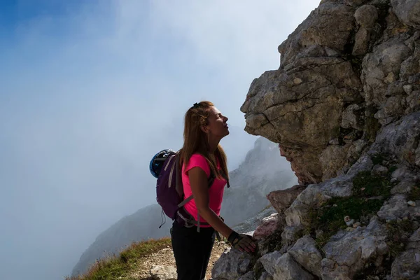 Woman hiker kissing a rock face in the Julian Alps, Slovenia, just under Mangart peak, after descending the via ferrata route. Misty clouds in the back. — Stock Photo, Image