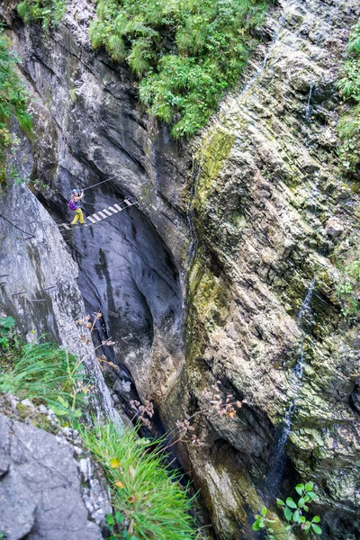 Mädchen überquert eine hölzerne Hängebrücke an der Postalmschlucht via ferrata, Österreich, wobei Wasser einen kleinen Wasserfall an den Canyonwänden bildet. vertikale Perspektive. — Stockfoto