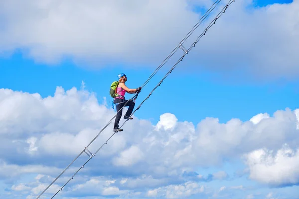 Cennet konseptine giden merdivenler. Gosau yakınlarındaki Donnerkogel dağlarında ferrata merdiveniyle çapraz dan tırmanan kadın, arkasında beyaz bulutlar ve mavi gökyüzü var..