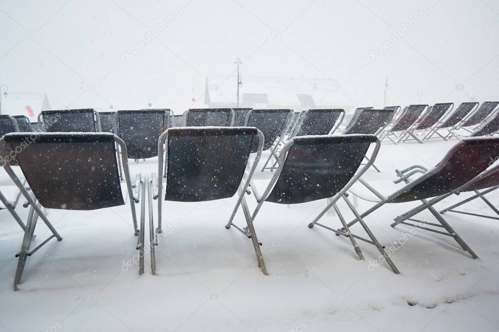 Empty sun lounger chairs out on a terrace during a Winter whiteout blizzard , Les Sybelles, France.