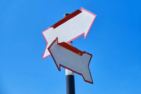 Blank arrow signs with two arrows pointing in different directions, on a bright blue sky.