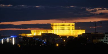 Romanya 'nın Bükreş kentindeki Parlamento Sarayı (Rumence Palatul Parlamentului) karanlık bulutların arasında gece aydınlandı. Bükreş 'in ufuk çizgisi, turistik mekan, tarihi yerler.