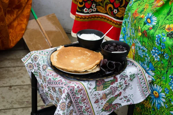 On the embroidered towel is a tray on it a plate with pancakes and two Krynki with sour cream and jam.