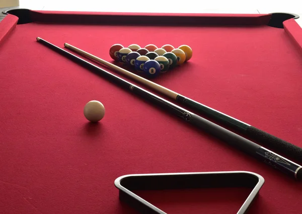 Colored and numbered Billiard balls on a red felt pool table with two cues, a cue ball and a black ball rack.