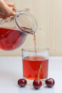 Bir el sürahi tutar ve bir bardağa vişne suyu döker.