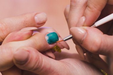 Bir kadın turkuaz jel cilası ile çivi boyar. Evde salon prosedürleri. Close