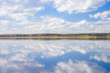 Mavi gökyüzü ve bulutlar nehre yansıdı. Su yüzeyinde dalgalanmalar. Ufukta orman