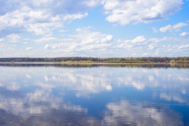 Mavi gökyüzü ve bulutlar nehre yansıdı. Su yüzeyinde dalgalanmalar. Ufukta orman