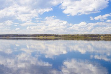 Mavi gökyüzü ve bulutlar nehre yansıdı. Su yüzeyinde dalgalanmalar. Ufukta orman