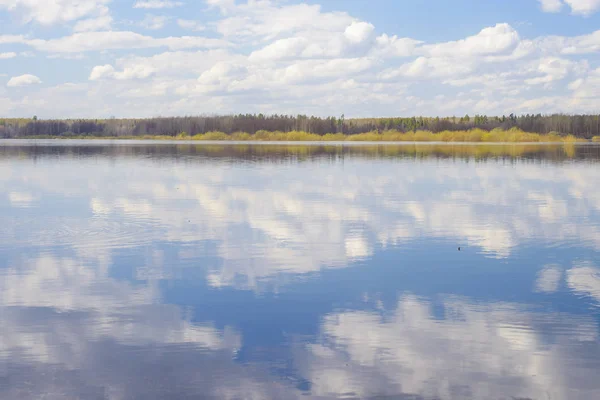 Blue sky and clouds reflected in the river. Ripples on the surface of the water. Forest on the horizon