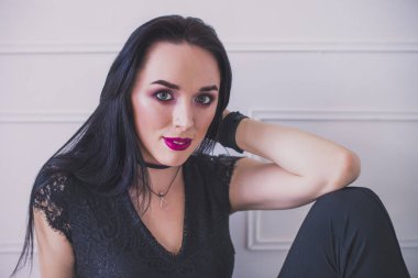 Siyah takım elbiseli seksi esmer model yerde oturuyor. beyaz bir duvara karşı. Yakın çekim portre