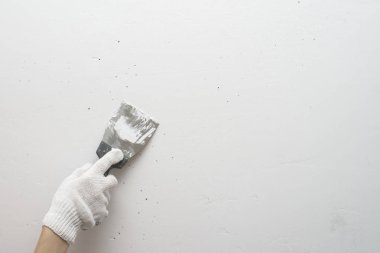 Working tool, spatula in hand against the background of a white wall, work plasterer. Putty walls with their own hands. clipart