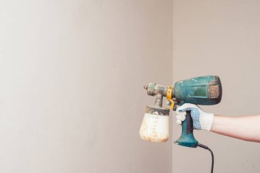 Elektrikli pulverizer boyayla kirlenmiş. Elinde yeşil sprey tabancası. Arka planda beyaz astarlı duvar.