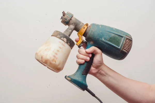 Electric pulverizer soiled in paint. Green spray gun in hand. White primed wall on the background. — Stock Photo, Image