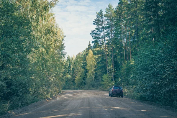 The car is standing on the side of a country dirt road in the forest. Landscape with tall trees. Edge of the forest in early autumn. — Stock Photo, Image