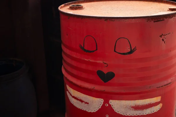 Old, red, iron barrel. Cartoon drawing of a female face on an old barrel.