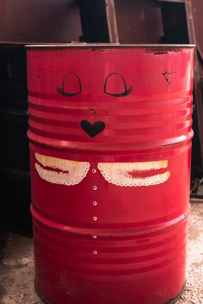 Old, red, iron barrel. Cartoon drawing of a female face on an old barrel.