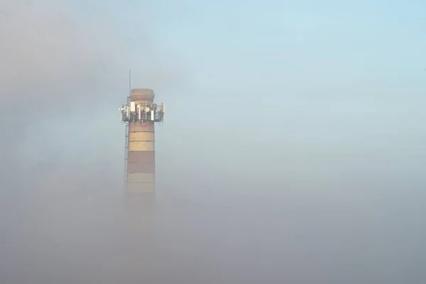 Die Heizungsrohre sind in Smog gehüllt. Ein Rohr lugt aus dem dichten Morgennebel. Luftverschmutzung. — Stockfoto