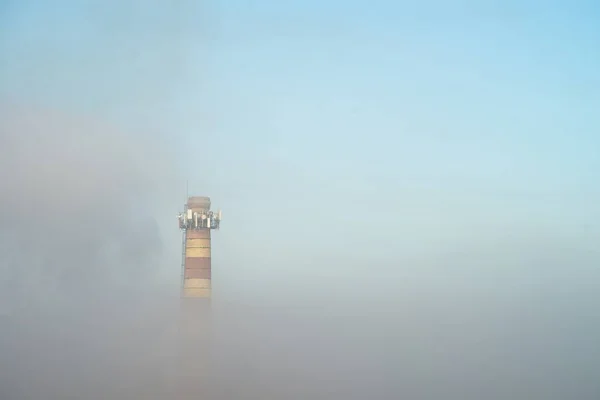 The boiler room pipe is shrouded in smog. A pipe peeps out of the dense morning fog. Air pollution. — Stock Photo, Image