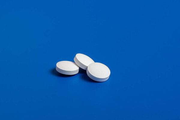 три белых круглых таблетки на синем фоне
