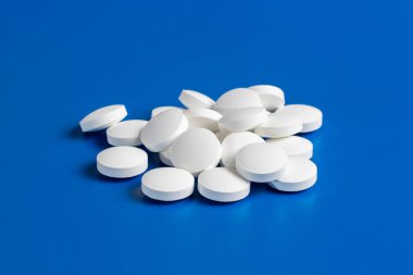 Beyaz yuvarlak haplar mavi arka planda, kaotik bir şekilde dağılmış..