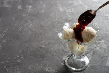 Beyaz vanilyalı dondurma topları ve tatlı bardağında ahududu reçeli. Koyu, sert betondan yapılmış bir masanın üzerinde süslenmiş dondurma. Kopyalama alanı.