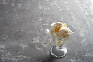 Tatlı olarak cam bardakta duran beyaz dondurma topları. Koyu sert betondan yapılmış bir masanın üzerinde süslenmiş dondurma..