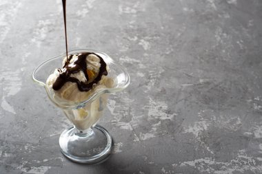 Tatlı bardağına çikolata soslu vanilyalı dondurma. Koyu, sert betondan yapılmış bir masanın üzerinde süslenmiş dondurma. Kopyala-uzayı düzlemi.