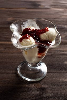 Tatlı bardağında ahududu reçeli vanilyalı dondurma. Kaba ahşaptan yapılmış eski bir masada süslenmiş dondurma. Kopyalama alanı.