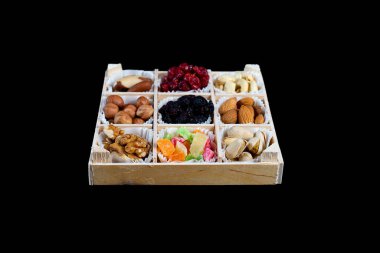 Siyah arka planda izole edilmiş ahşap bir kutuda çeşitli kurutulmuş meyve ve fındıklar. Kuru üzüm, şeker, kiraz, Brezilya fındığı, fındık, ceviz, badem, fıstık, fıstık..