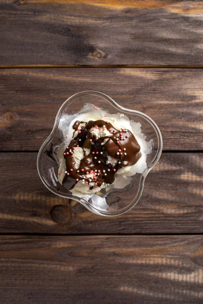 Білі кульки ванільного морозива залиті шоколадною начинкою в десертному келиху. Прикрашене морозиво на старому столі з грубого дерева. Планшет Copyspace . — стокове фото
