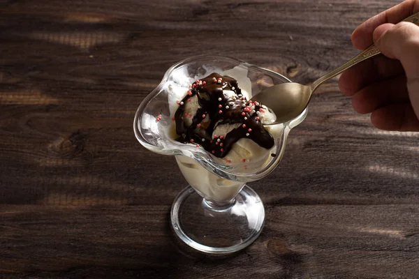 Білі кульки ванільного морозива залиті шоколадною начинкою в десертному келиху з ложкою. Прикрашене морозиво на старому столі з грубого дерева. Копіспазмі . — стокове фото