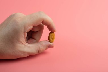 Parmakların pembe arka planda tek badem tohumu tutması