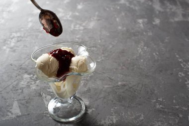 Beyaz vanilyalı dondurma topları ve tatlı bardağında ahududu reçeli. Koyu, sert betondan yapılmış bir masanın üzerinde süslenmiş dondurma. Kopyalama alanı.