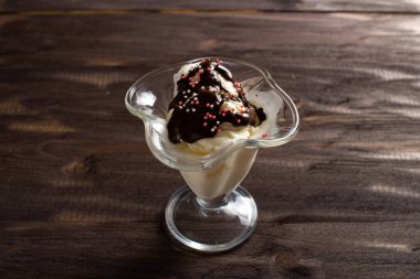 Tatlı bardağına çikolata soslu vanilyalı dondurma. Kaba ahşaptan yapılmış eski bir masada süslenmiş dondurma. Kopyalama alanı.
