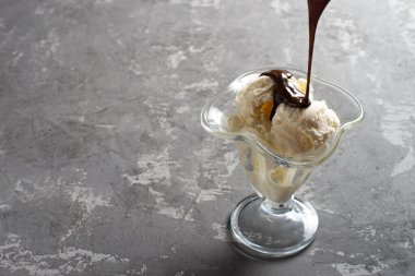 Tatlı bardağına çikolata soslu vanilyalı dondurma. Koyu, sert betondan yapılmış bir masanın üzerinde süslenmiş dondurma. Kopyala-uzayı düzlemi.