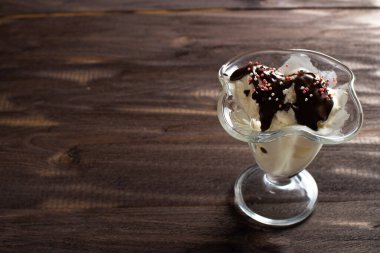 Tatlı bardağına çikolata soslu vanilyalı dondurma. Kaba ahşaptan yapılmış eski bir masada süslenmiş dondurma. Kopyalama alanı.
