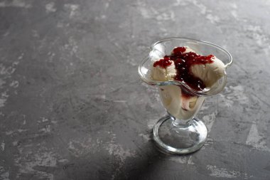 Tatlı bardağında ahududu reçeli vanilyalı dondurma. Koyu, sert betondan yapılmış bir masanın üzerinde süslenmiş dondurma. Kopyalama alanı.