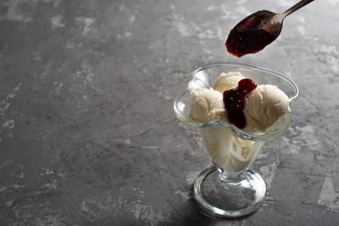 Beyaz vanilyalı dondurma topları ve tatlı bardağında ahududu reçeli. Koyu, sert betondan yapılmış bir masanın üzerinde süslenmiş dondurma. Kopyalama alanı.