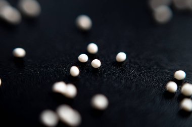 Siyah arka planda beyaz şekerleme topları şeklinde serpiştirilmiş. Yakın çekim, makro.