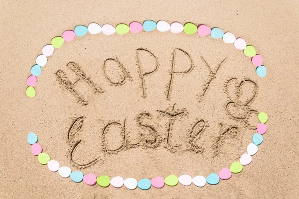 Fondo de letras de Pascua feliz con huevos en la playa de arena — Foto de Stock