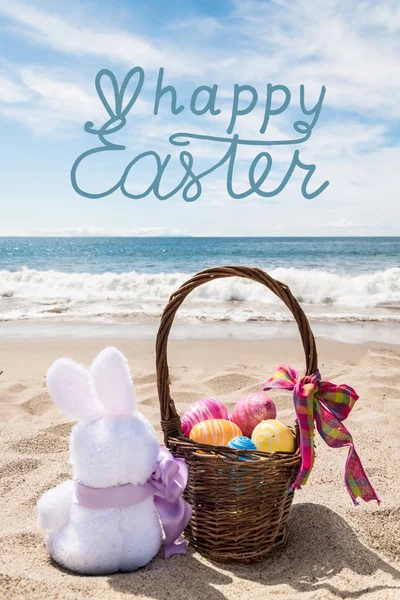 Conejo de Pascua con cesta y huevos de color en la playa del océano — Foto de Stock