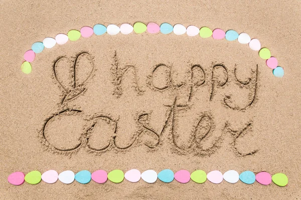 Fondo de letras de Pascua feliz con huevos en la playa de arena — Foto de Stock