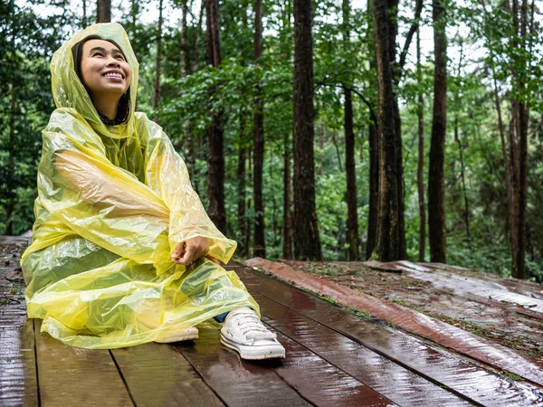 Mujer asiática feliz vistiendo impermeable amarillo sentarse en un piso de madera — Foto de Stock