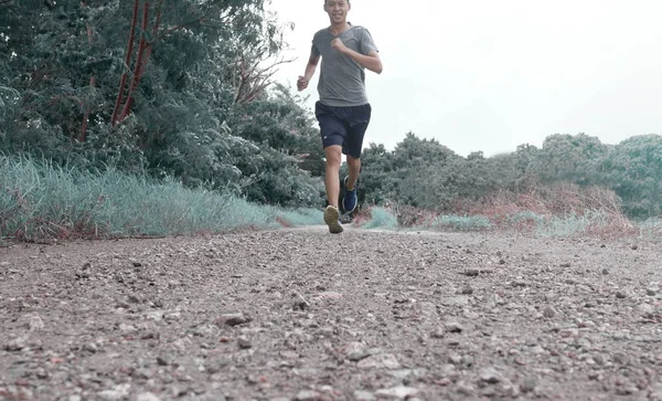 Asian young man is jogging on dirt road in the park. Healthy lif — Stock Photo, Image