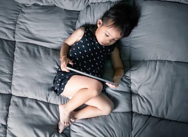 Asiatisk liten flicka tittar på laptop på deras säng. Grabben är beroende av — Stockfoto