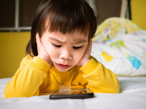 Küçük Asyalı kız yataklarında akıllı telefon izliyor. Çocuk bağımlı. — Stok fotoğraf