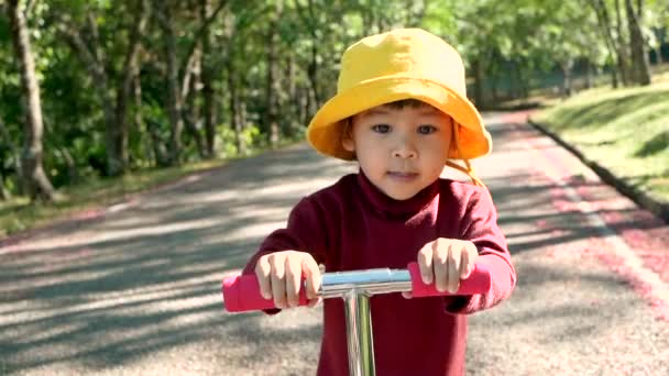 陽気子供の女の子は夏の公園で道路上のスクーターに乗っています 幸せな家庭と子供時代の概念 — ストック動画