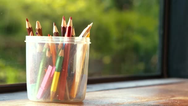 手把彩色铅笔放在一个塑料圆盒里 放在窗边的木制桌子上 阳光照射在绿色的背景上 — 图库视频影像